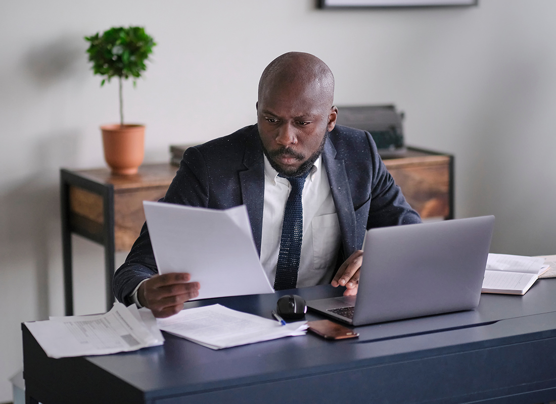 Business Insurance - Business Professional Reviewing Documents and Using Laptop at His Office